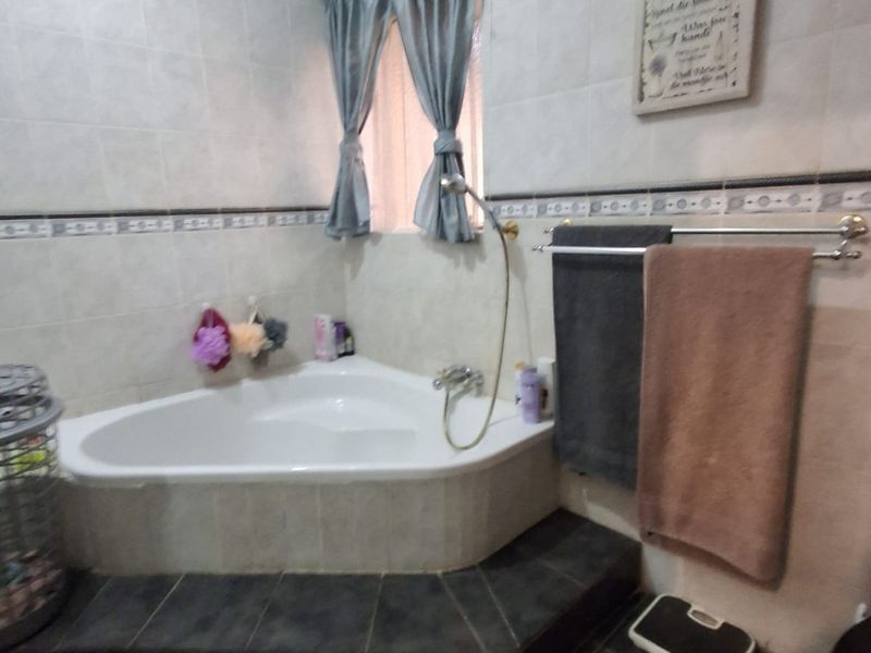 A bathroom featuring a corner bathtub with tiled surround, wall-mounted towel rail, and neutral wall tiling.