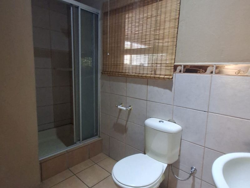 A functional bathroom featuring a shower enclosure, toilet, and pedestal basin with neutral ceramic tiling throughout.