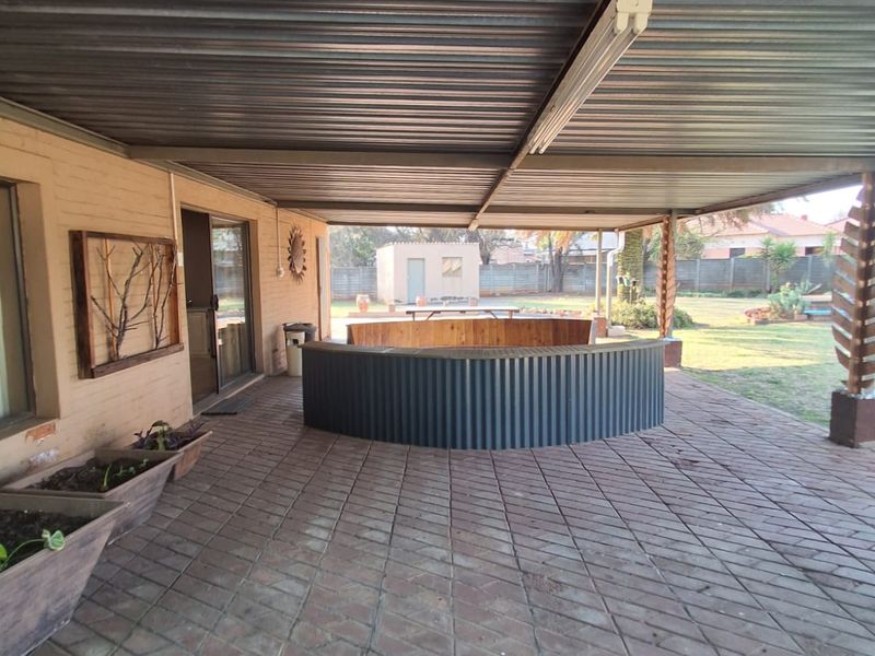 Covered outdoor patio area featuring a built-in bar counter, corrugated metal roofing, and paved flooring, overlooking the rear garden.