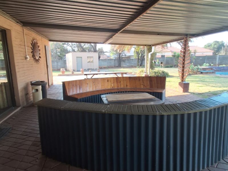 Covered outdoor patio area featuring a corrugated metal roof, paved flooring, and a built-in curved seating structure overlooking the garden.