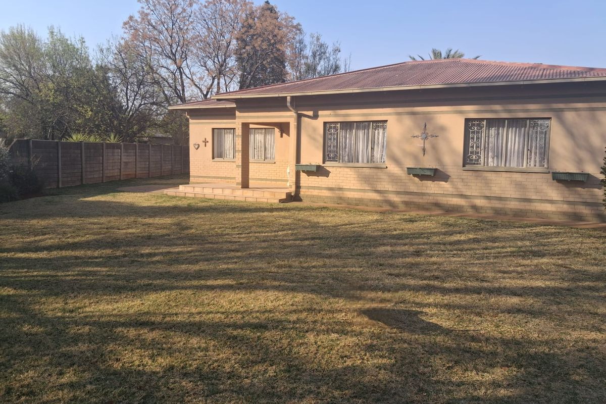 Rear view of a single-story brick house featuring a corrugated metal roof, security bars on windows, and a spacious backyard with a concrete patio.