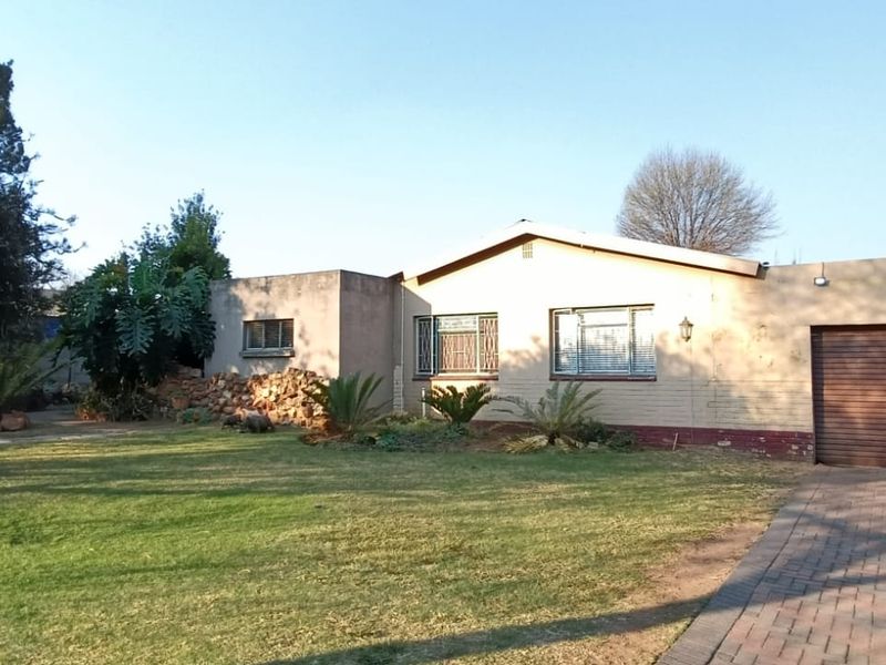 Front view of a single-story house featuring a paved driveway, double garage, and established garden area.