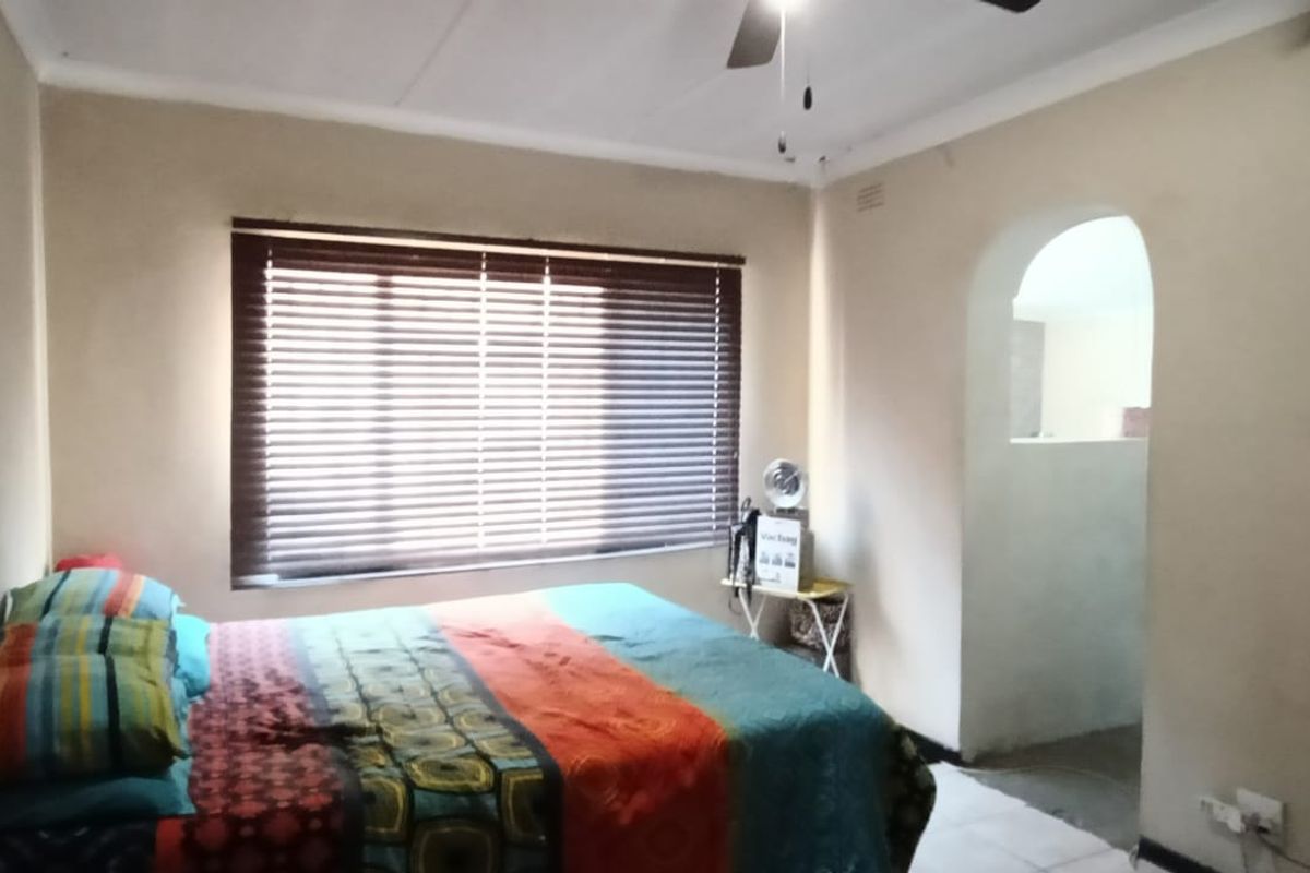 A bedroom featuring a ceiling fan, venetian blinds, and an arched doorway leading to an adjacent space.