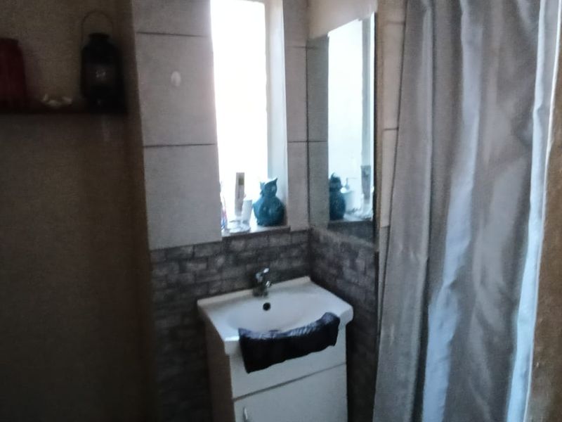 A functional bathroom featuring a pedestal basin with tiled splashback and a shower area with a curtain.