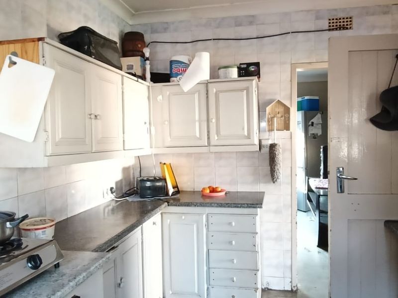 A dated kitchen featuring original cabinetry, tiled splashbacks, and a gas hob, offering significant potential for modernization and renovation.