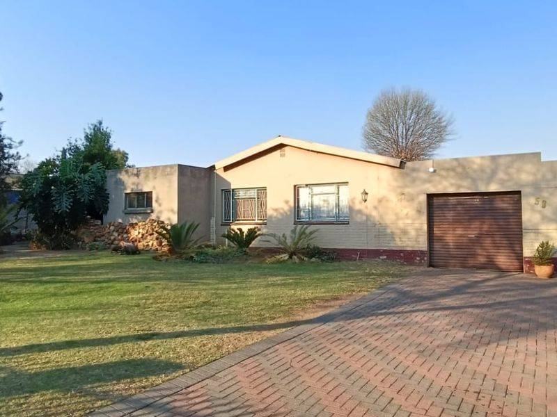 Front elevation of a single-story house featuring a double garage, paved driveway, and established garden area.