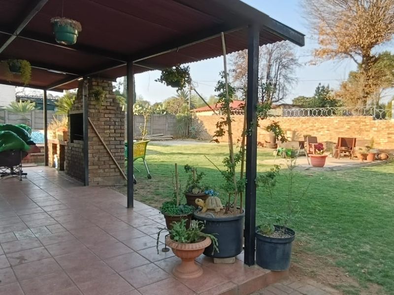 Covered outdoor patio featuring a built-in brick braai, tiled flooring, and direct access to a spacious rear garden area.