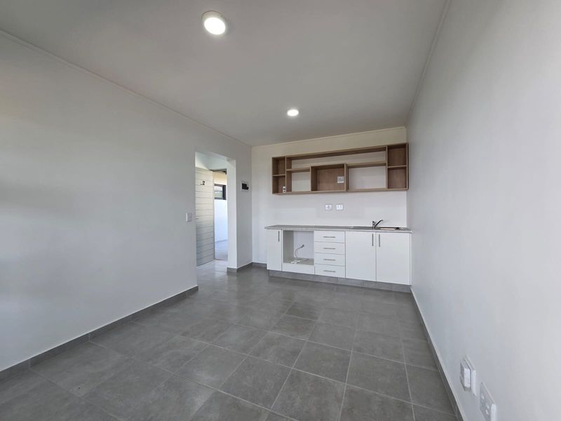 A clean, modern, and empty kitchen area featuring white cabinetry, open shelving, a stainless steel sink, and neutral grey floor tiles.