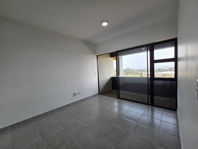 A bright, empty bedroom featuring neutral tiled flooring, a modern sliding glass door leading to a balcony, and clean white walls.