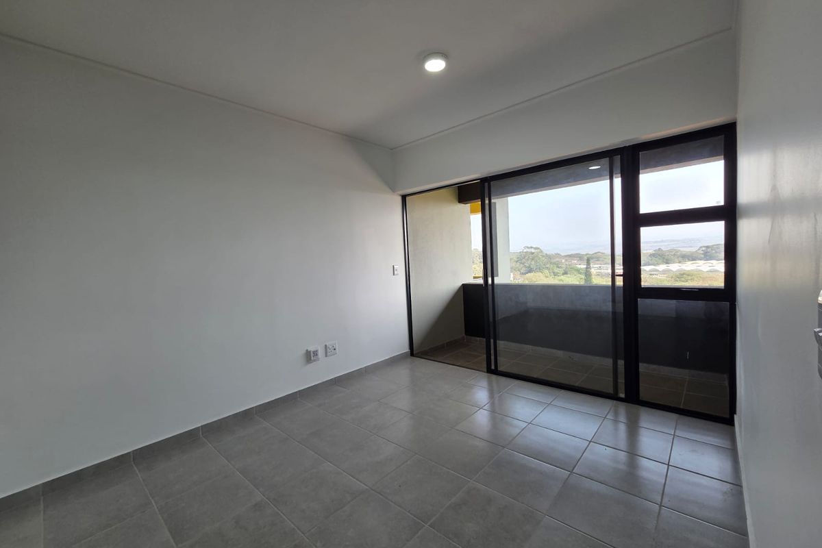 A bright, empty bedroom featuring neutral tiled flooring, a modern sliding glass door leading to a balcony, and clean white walls.