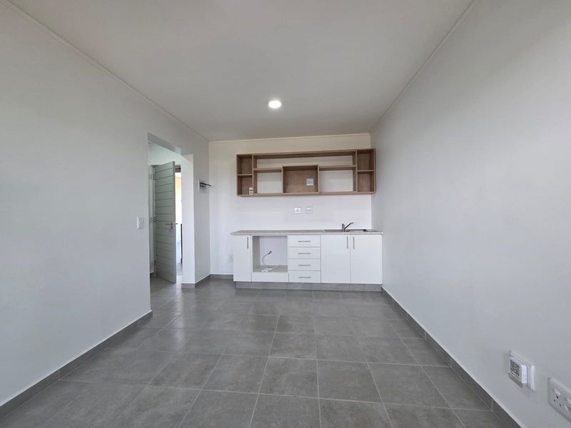 A clean, modern kitchen area featuring white base cabinetry, open wooden shelving, a stainless steel sink, and neutral grey floor tiles.