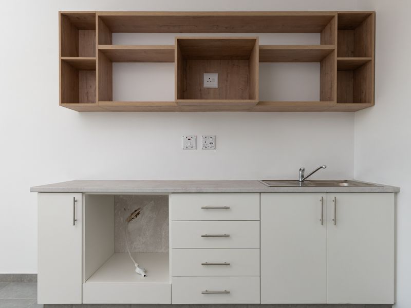 A clean, modern scullery or utility area featuring white cabinetry, wood-look open shelving, a stainless steel sink, and a dedicated appliance cavity.