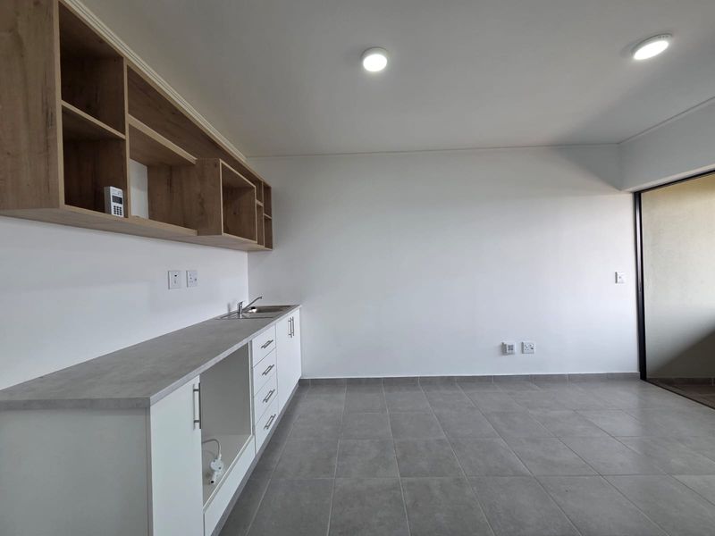 A clean, modern kitchen area featuring built-in cabinetry, open shelving, a stainless steel sink, and neutral tiled flooring in an open-plan layout.