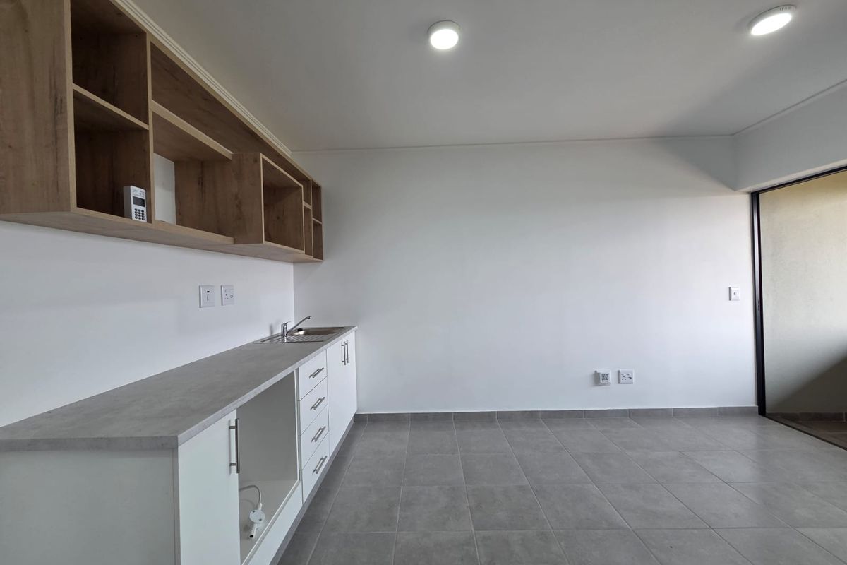 A clean, modern kitchen area featuring built-in cabinetry, open shelving, a stainless steel sink, and neutral tiled flooring in an open-plan layout.