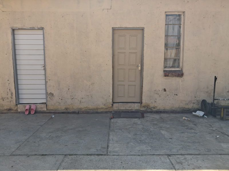 Rear exterior view of the property featuring a concrete paved area, a panel door, a security gate, and a window with security bars.