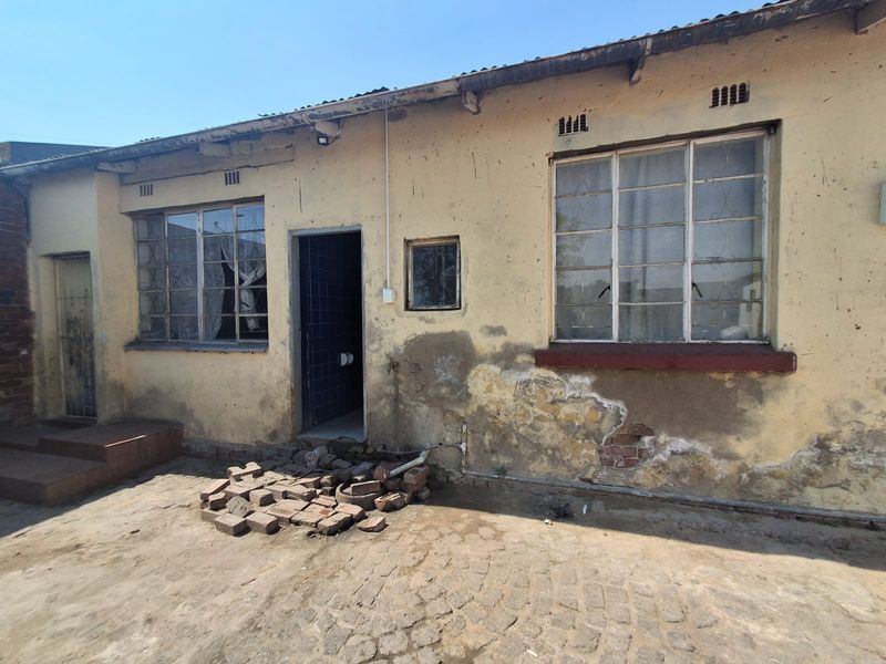 Rear exterior view of the property showing significant wear to the wall plaster, steel-framed windows, and paved outdoor area.