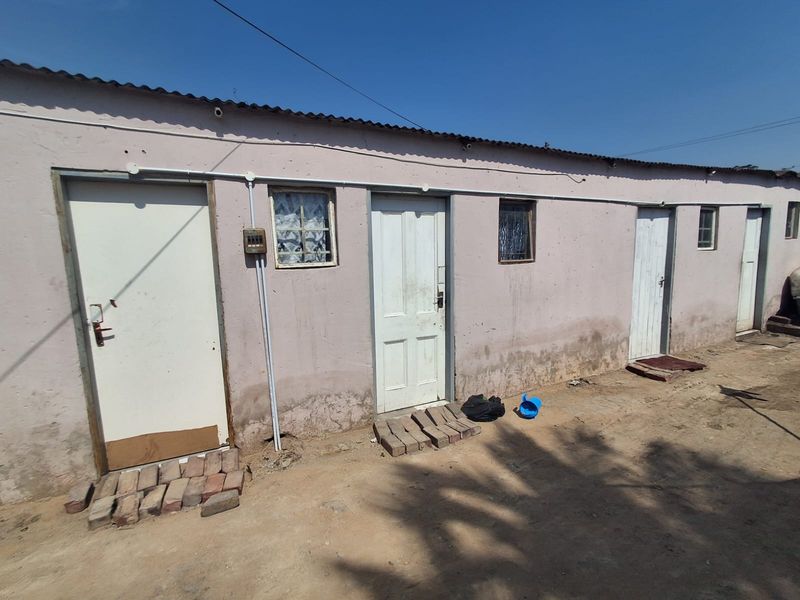 Exterior view of a multi-unit residential structure featuring a corrugated metal roof, multiple entrance doors, and weathered plaster walls with visible signs of wear.