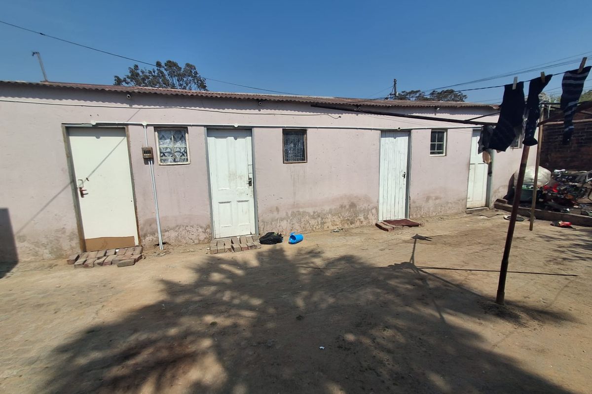 Rear exterior view of a single-story residential structure featuring multiple access doors and small windows, showing signs of significant exterior wall weathering.