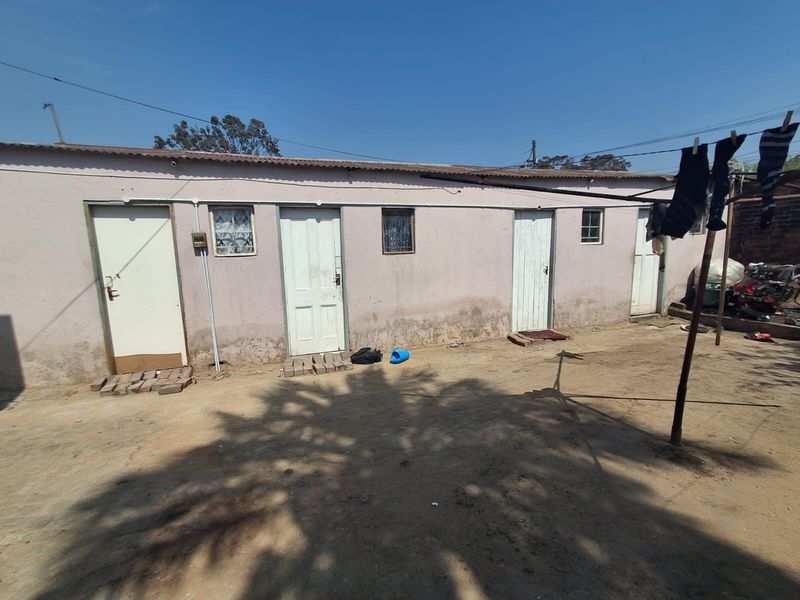 Rear exterior view of a single-story residential structure featuring multiple access doors and small windows, showing signs of significant exterior wall weathering.