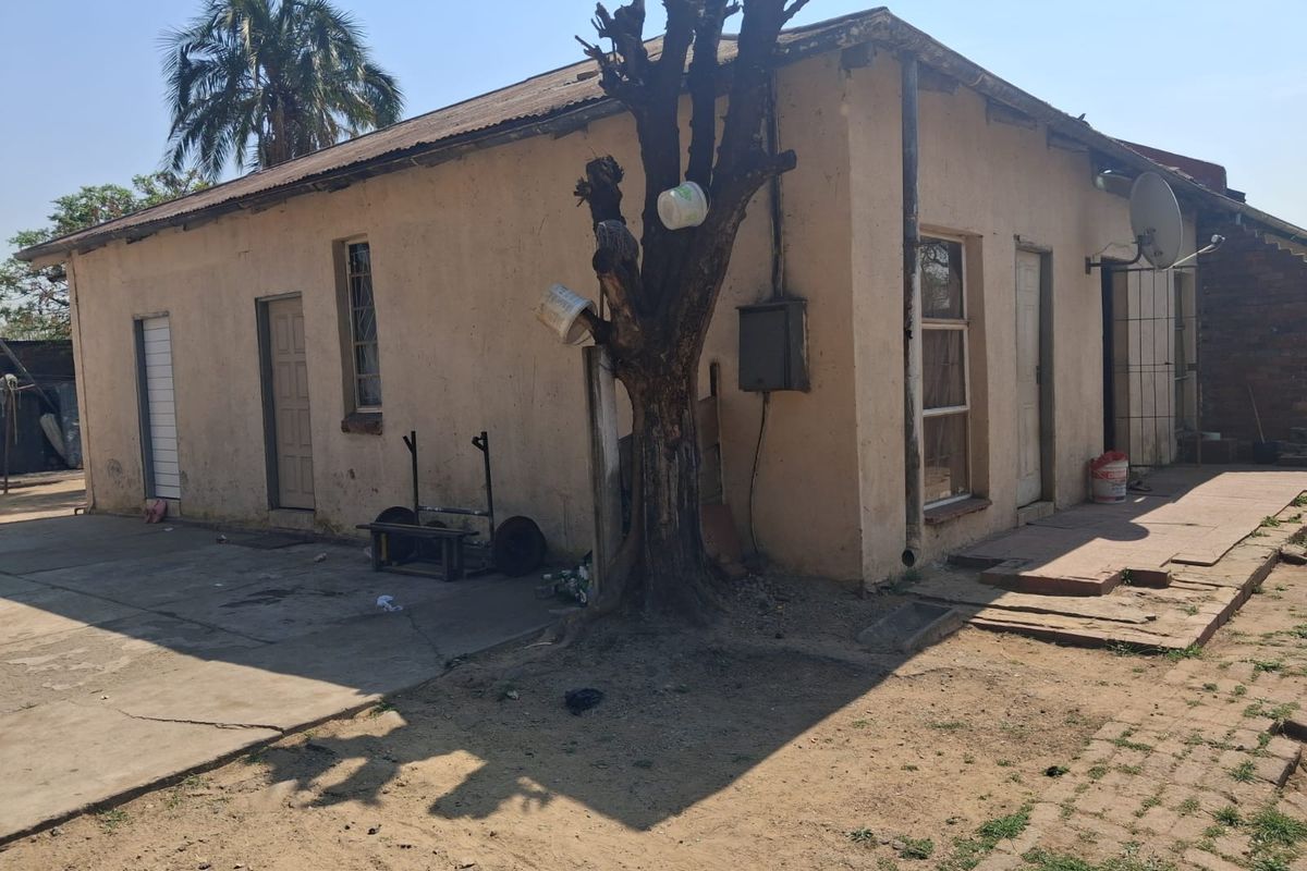 Rear exterior view of the property showing the building facade, concrete paving, and roof structure in need of maintenance.