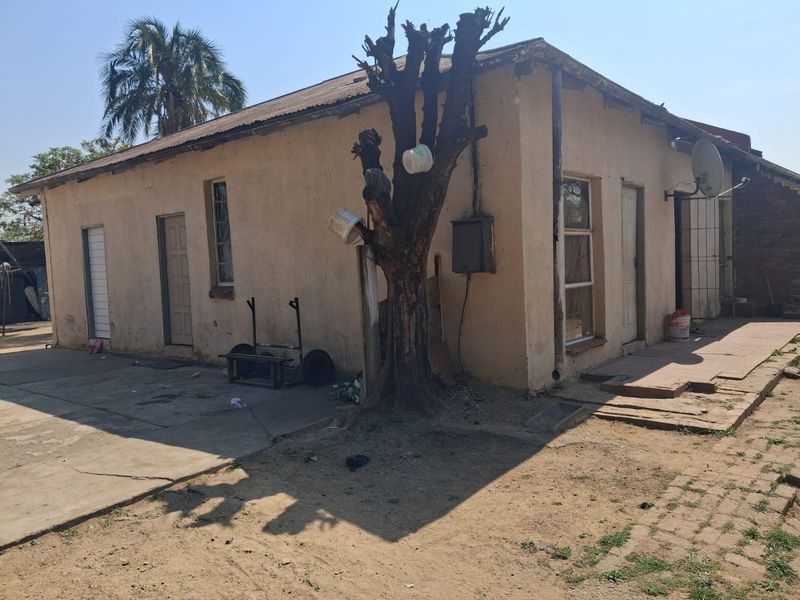 Rear exterior view of the property showing the building facade, concrete paving, and roof structure in need of maintenance.