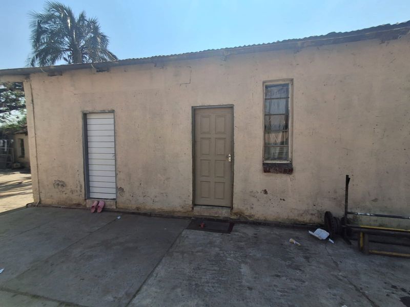 Rear exterior view of the property featuring a concrete patio area, weathered plaster walls, and basic door and window access points.