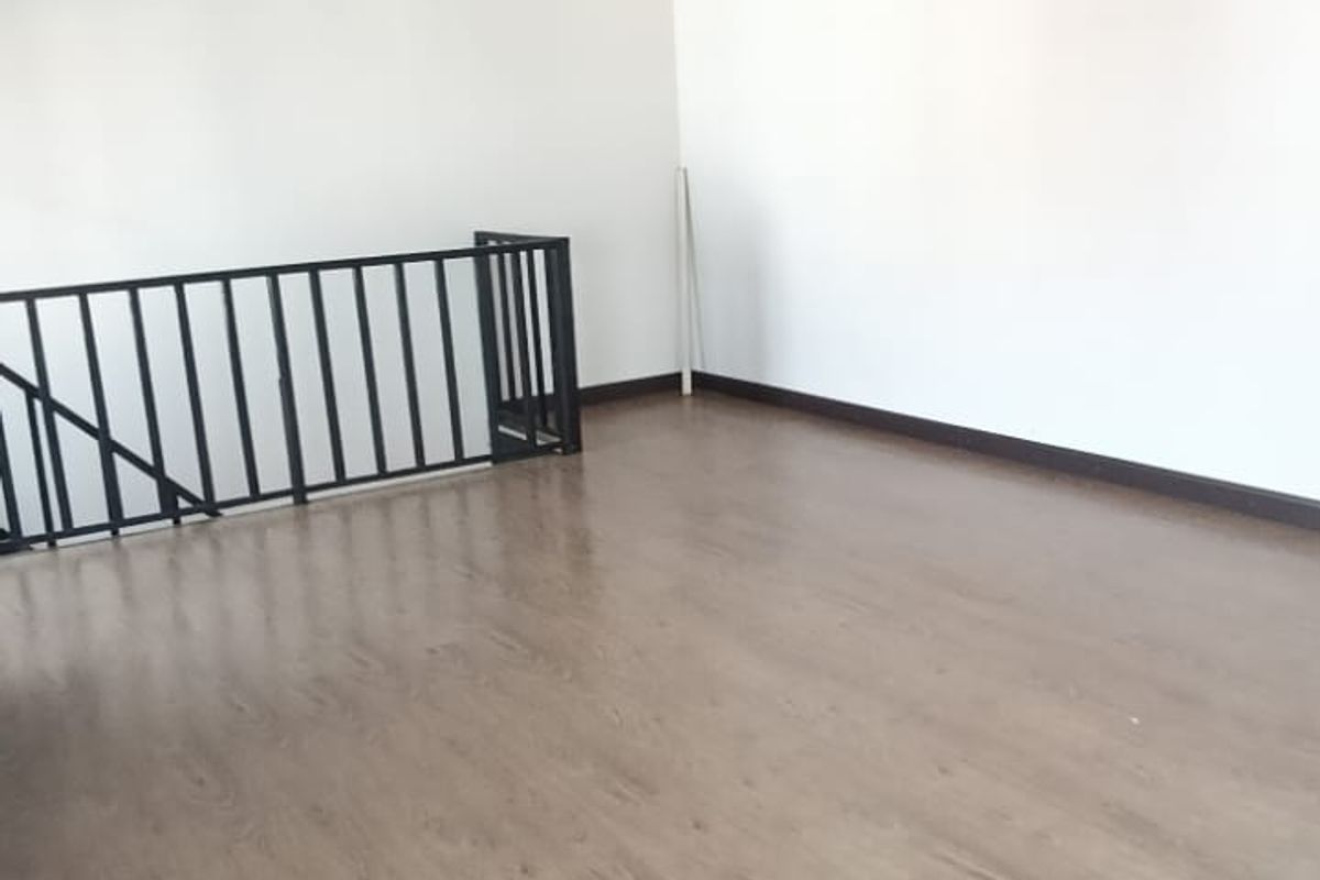 A spacious, empty living area featuring modern laminate flooring, clean white walls, and a black metal balustrade overlooking a lower level.