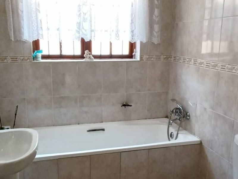 A functional bathroom featuring a built-in bathtub, pedestal basin, and toilet, finished with neutral ceramic wall and floor tiles.