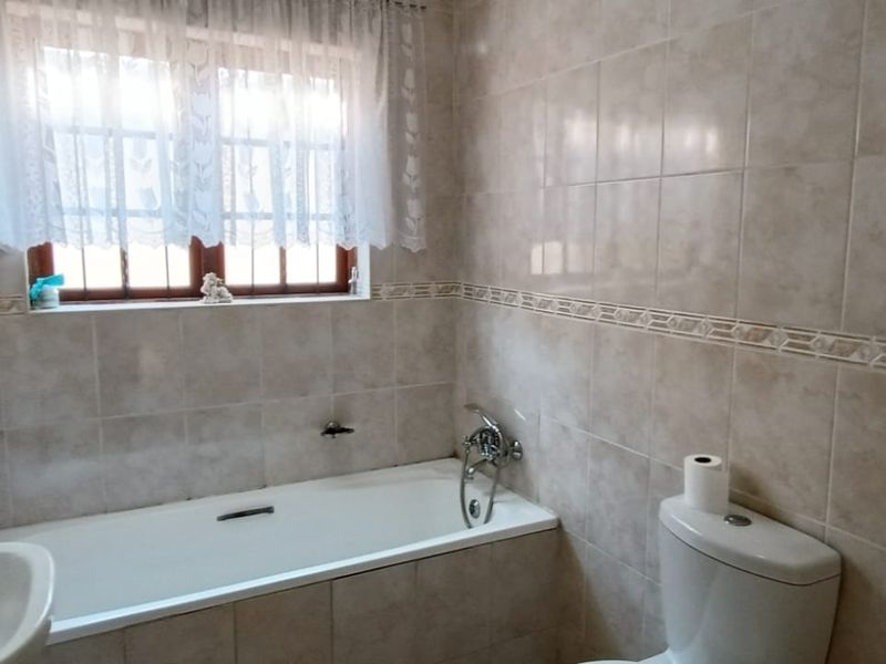 A functional bathroom featuring a bathtub, toilet, and washbasin with neutral wall tiling and a window for natural light.