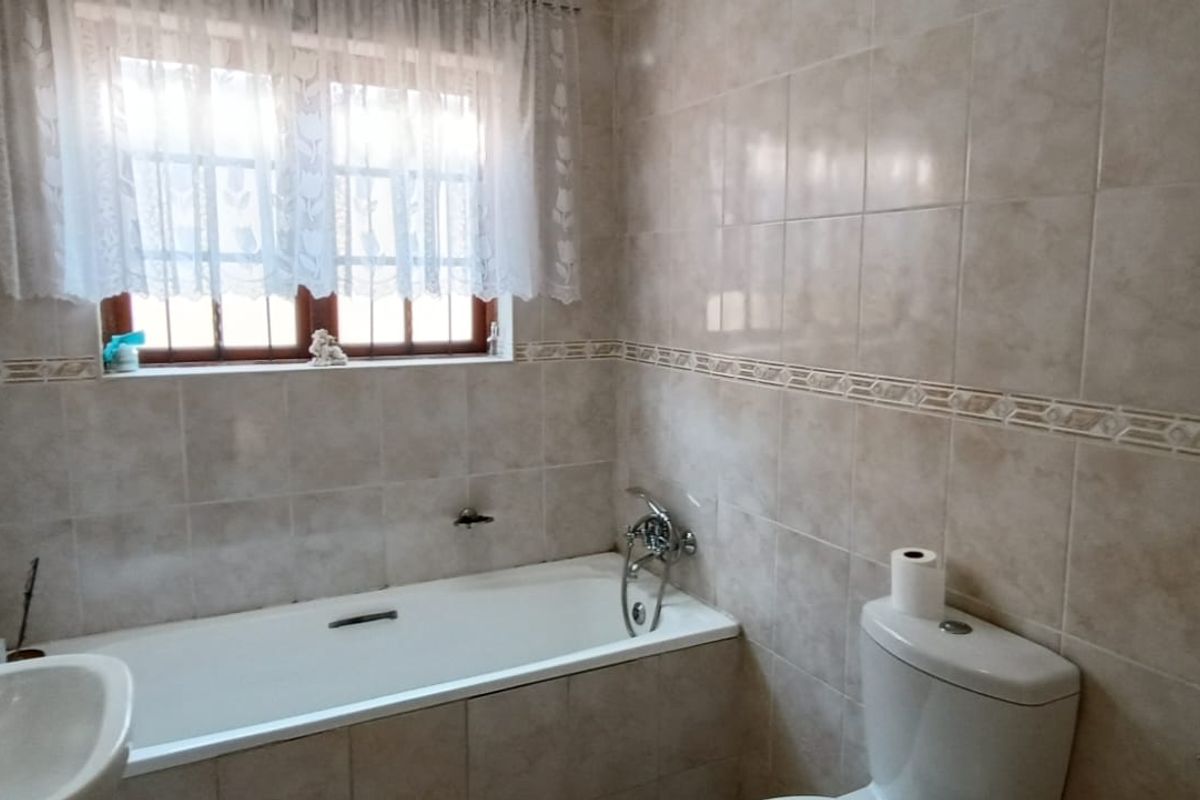 A functional bathroom featuring a bathtub, toilet, and washbasin with neutral wall tiling and a window for natural light.