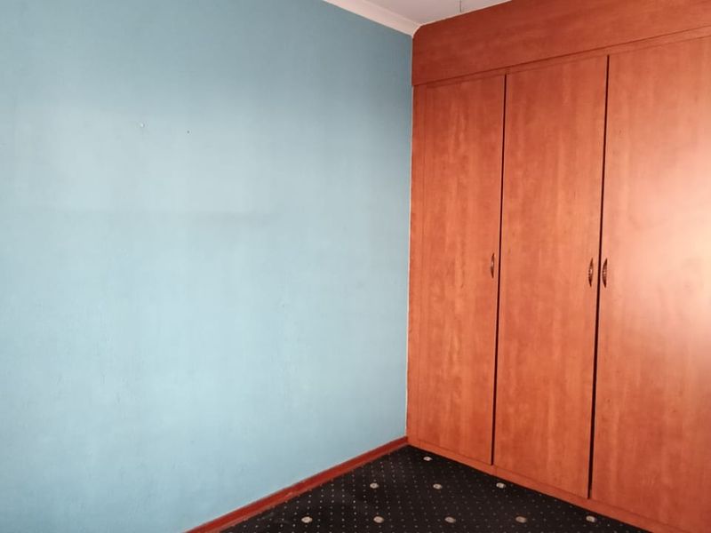 A bedroom featuring built-in wooden wardrobes and carpeted flooring, presenting a blank canvas for potential interior updates.