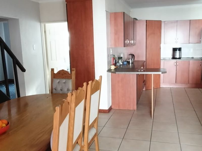Open plan living and dining area featuring tiled flooring, built-in kitchen cabinetry, and a staircase leading to the upper level.