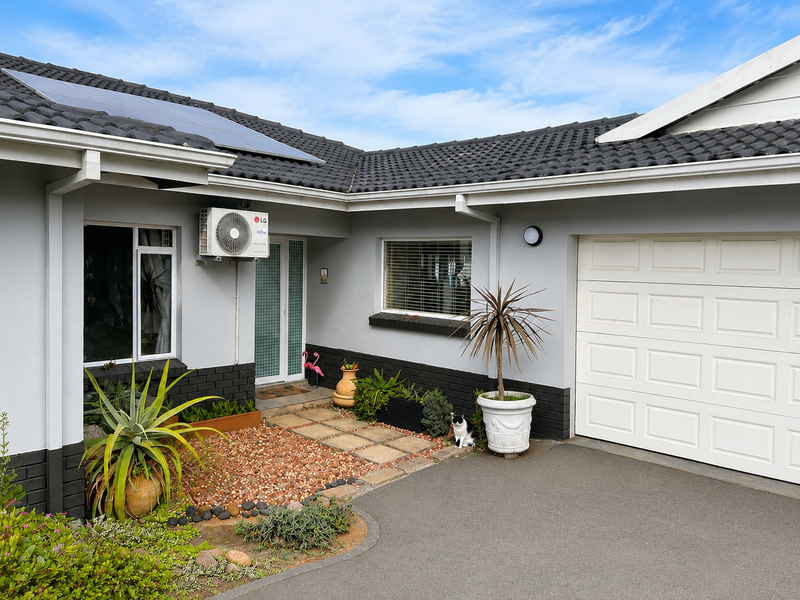 Front elevation of a well-maintained house featuring a paved driveway, sectional garage door, solar panels, and a neat low-maintenance garden.