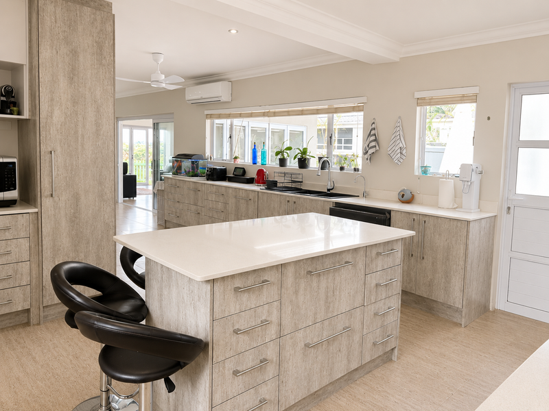 Modern kitchen featuring a central island with quartz countertops, ample built-in cabinetry, double sink, and integrated air conditioning, flowing into an adjacent living space.