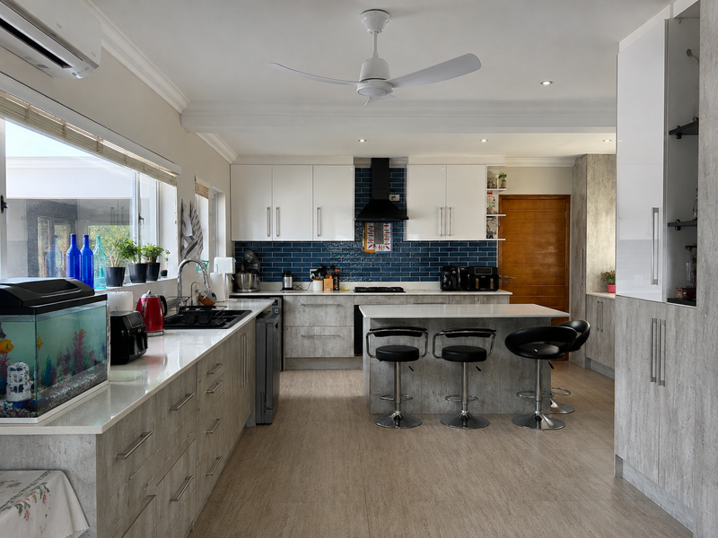 Modern kitchen featuring stone countertops, a central island with breakfast bar seating, blue subway tile backsplash, and integrated cabinetry with high-quality finishes.