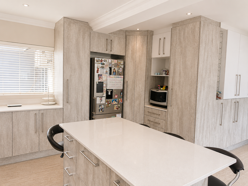 Modern kitchen featuring light wood-grain cabinetry, a central island with quartz countertops, and integrated storage solutions in a bright, well-maintained space.