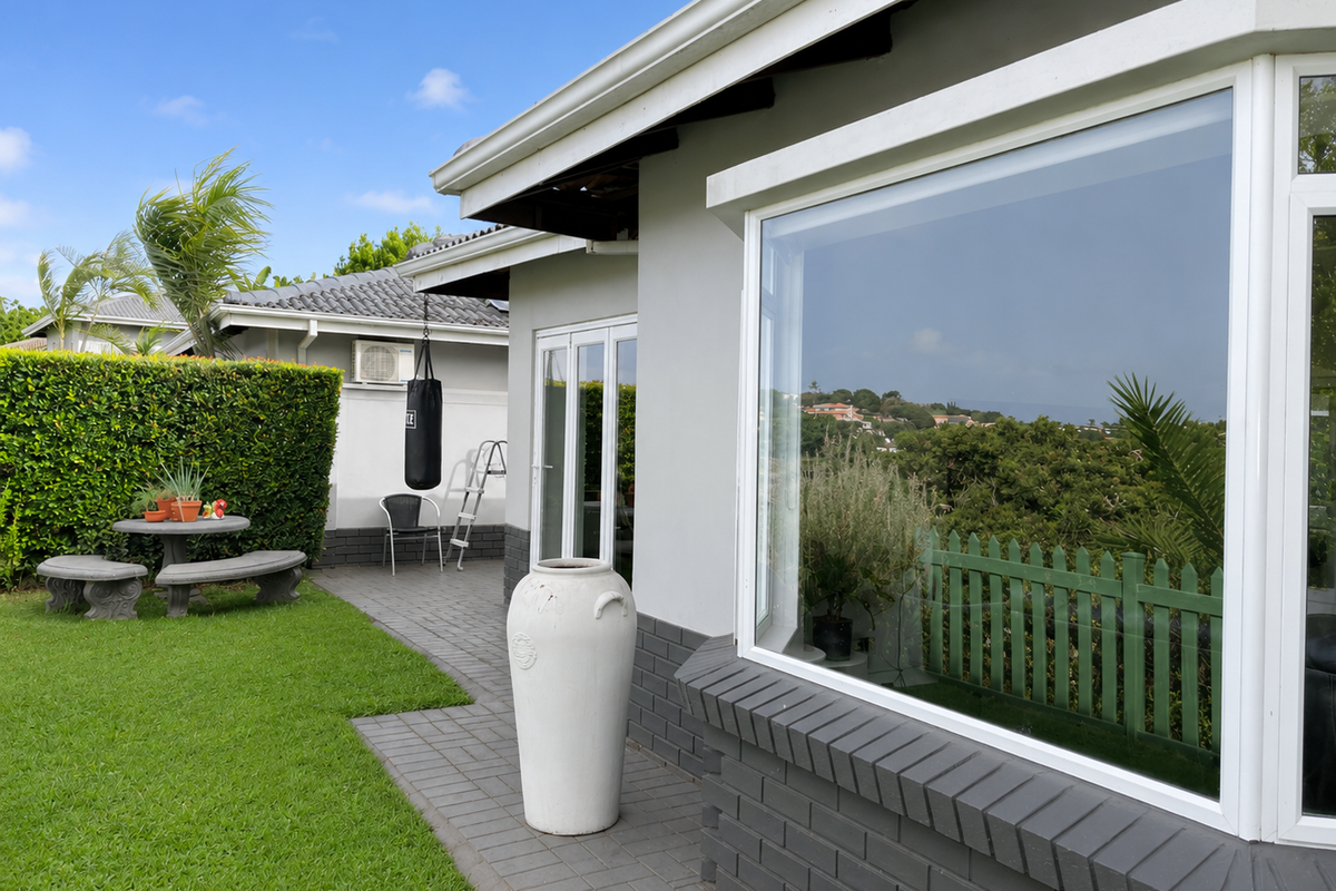 A well-maintained rear exterior featuring a paved patio, manicured lawn, and a large bay window overlooking the garden.