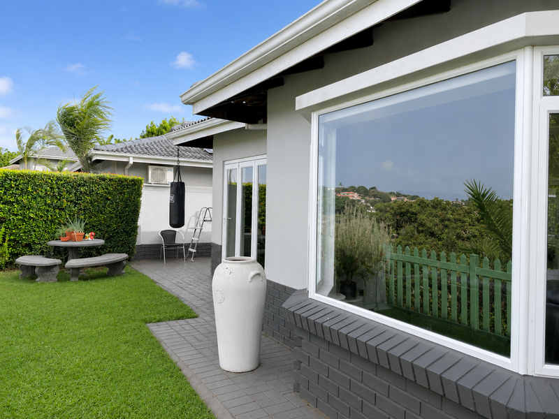 A well-maintained rear exterior featuring a paved patio, manicured lawn, and a large bay window overlooking the garden.