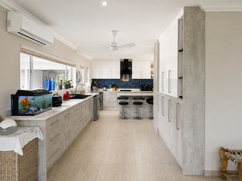 Modern kitchen featuring extensive built-in cabinetry, stone countertops, a blue subway tile backsplash, and integrated appliances, complemented by tiled flooring and air conditioning.