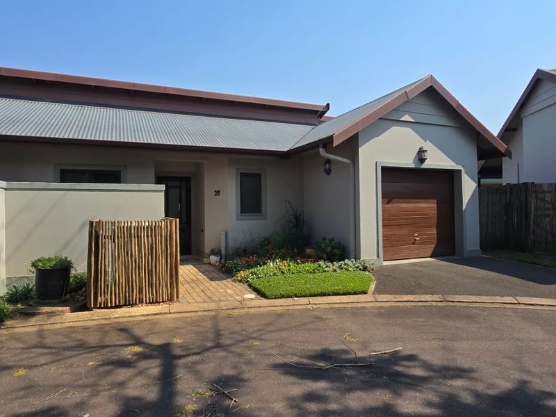 Front elevation of a townhouse featuring a single garage, paved driveway, and a neat entrance walkway with landscaped garden beds.