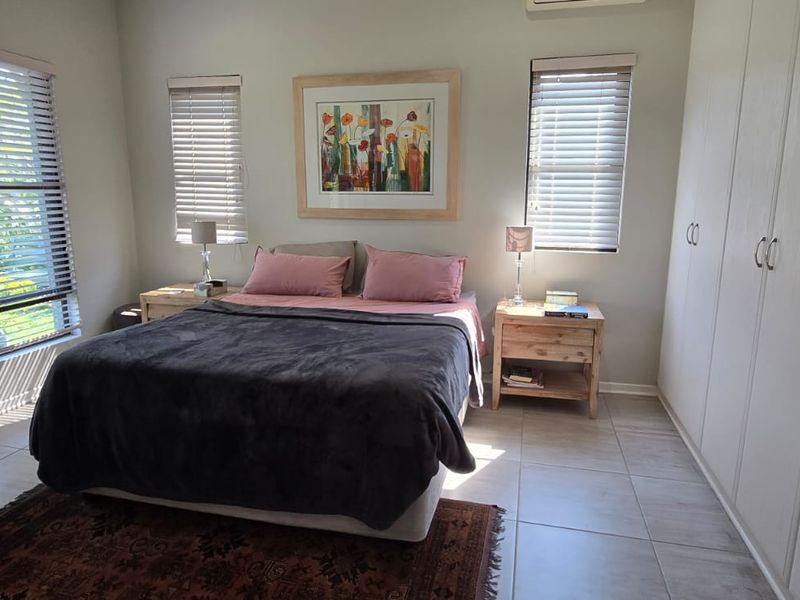 A well-maintained bedroom featuring tiled flooring, ample built-in cupboard space, venetian blinds, and an integrated air conditioning unit.