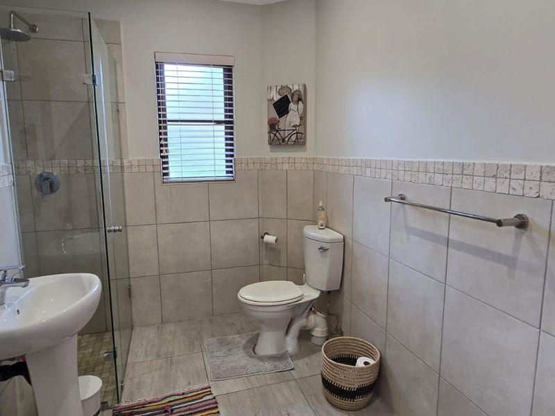 A functional bathroom featuring a pedestal basin, a glass-enclosed shower, and neutral wall and floor tiling.