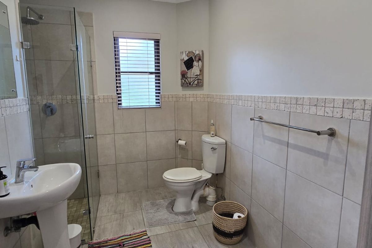 A functional bathroom featuring a pedestal basin, a glass-enclosed shower, and neutral wall and floor tiling.