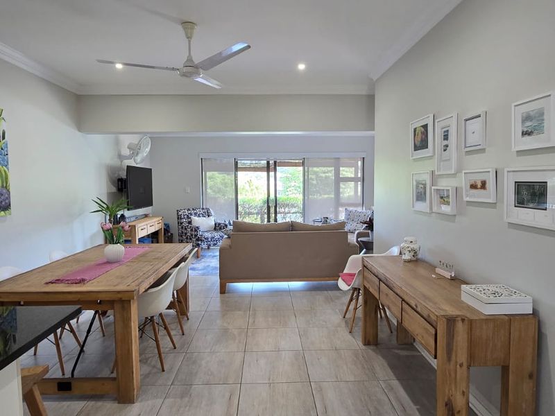 Spacious open-plan living and dining area featuring neutral tiled flooring, a ceiling fan, and large sliding glass doors leading to the outdoor space.