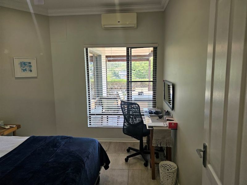 A bedroom featuring tiled flooring, a wall-mounted split-system air conditioner, and venetian blinds overlooking an outdoor patio area.