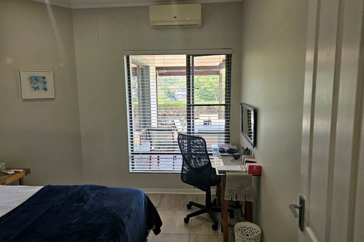 A bedroom featuring tiled flooring, a wall-mounted split-system air conditioner, and venetian blinds overlooking an outdoor patio area.