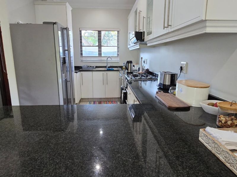A functional kitchen featuring granite countertops, white cabinetry, a gas hob, and an integrated sink area with a window for natural light.