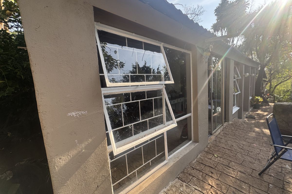 Rear exterior view of the property featuring a paved patio area and windows with integrated security bars, showing a cracked glass pane.