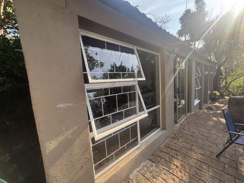 Rear exterior view of the property featuring a paved patio area and windows with integrated security bars, showing a cracked glass pane.