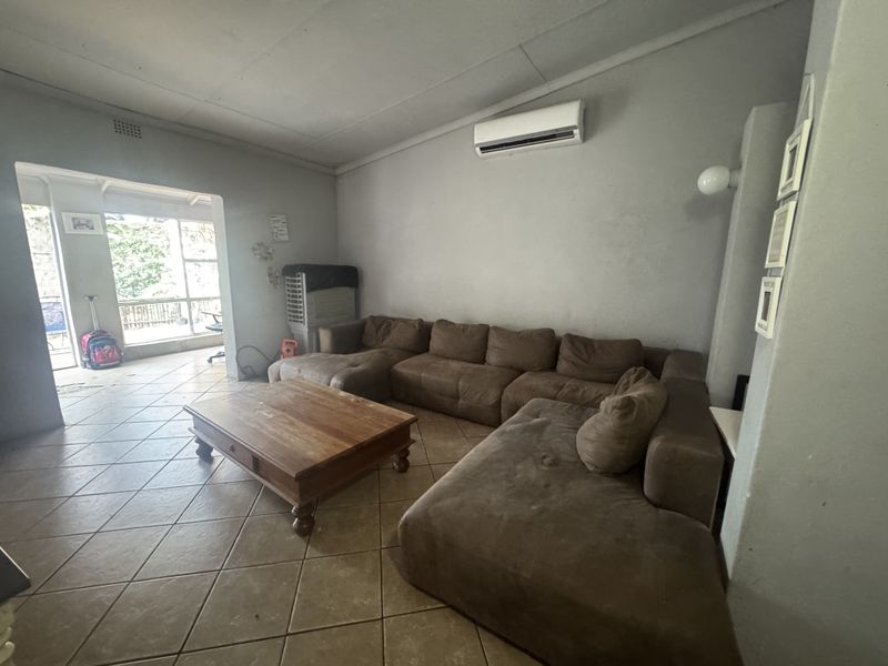 A spacious living room featuring ceramic floor tiles, a wall-mounted air conditioning unit, and direct access to an adjoining patio area.